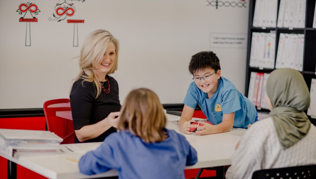 A Mathnasium teacher sits at a table and teaches math to three students via a card game.
