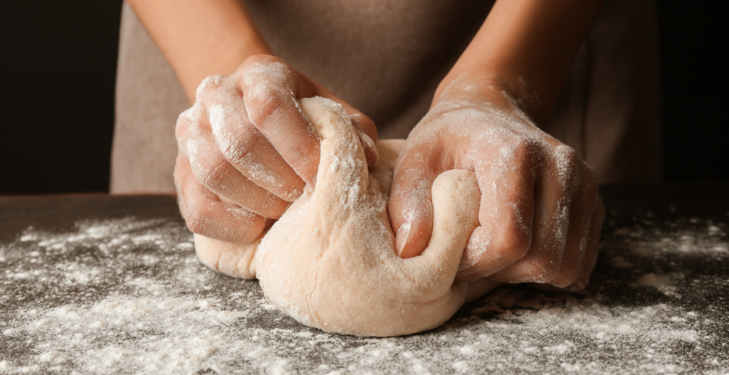Two hands knead raw dough. 