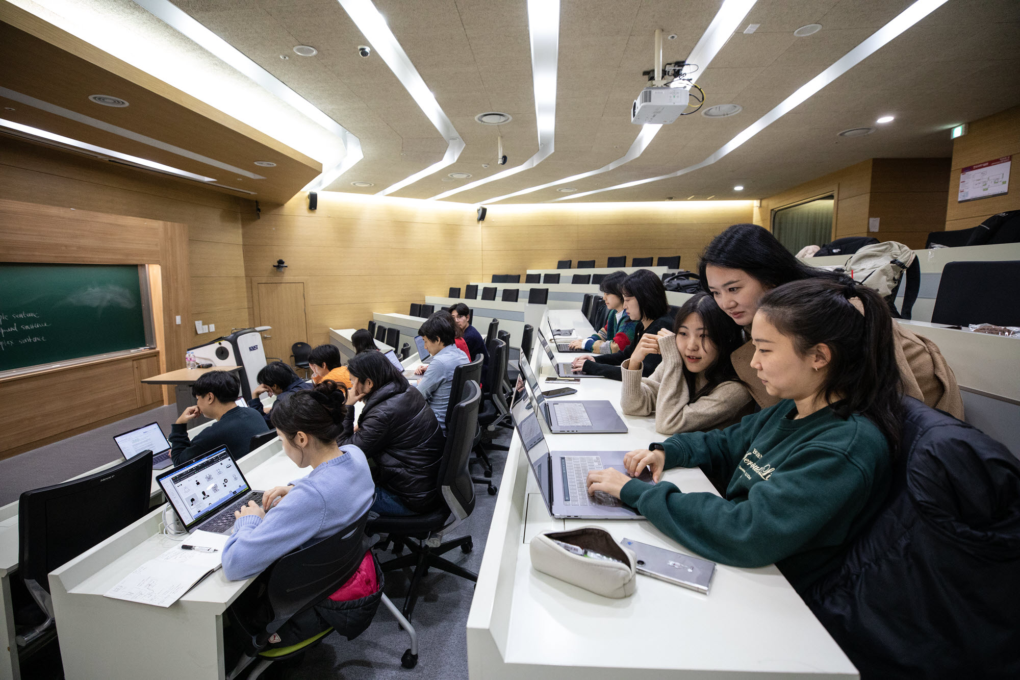 这是一张女教授与两名坐在电脑前的女学生在韩国高级科学技术学院演讲厅交谈的照片。 