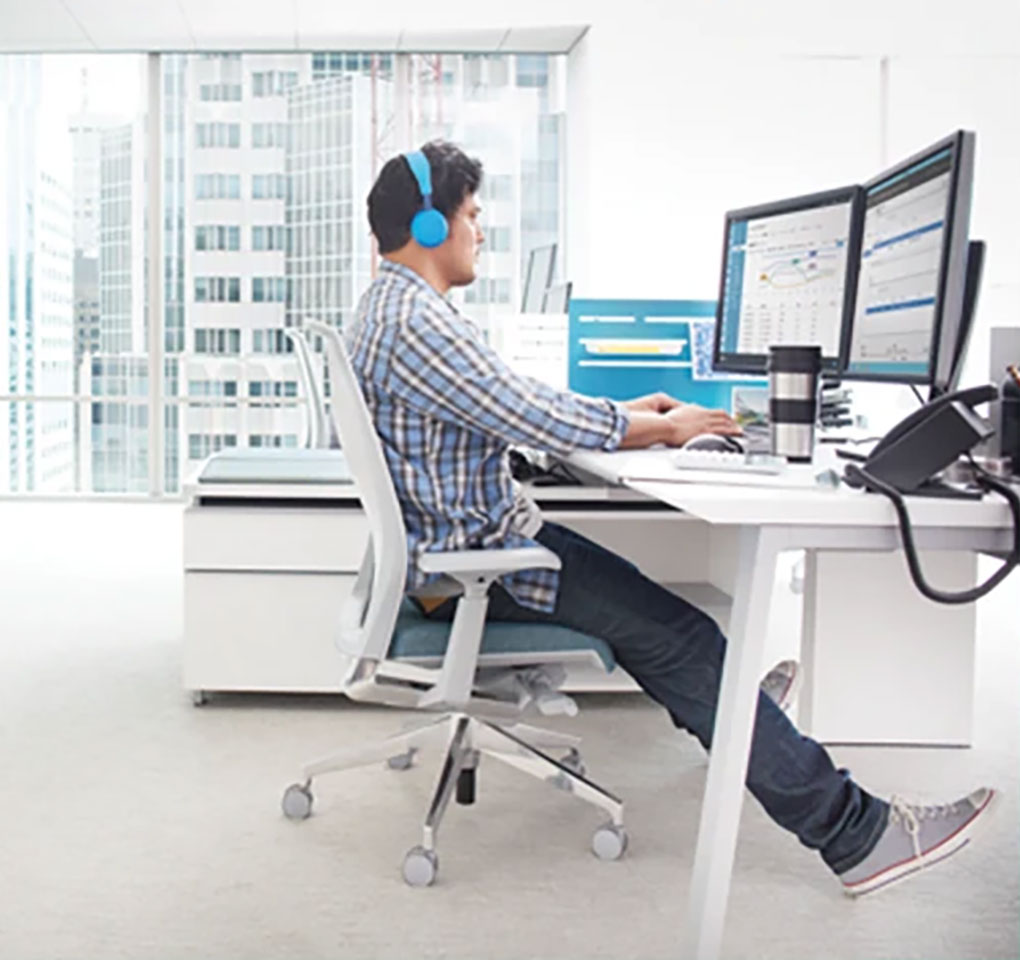 Man wearing headphones working in an office at a desktop computer with multiple screens