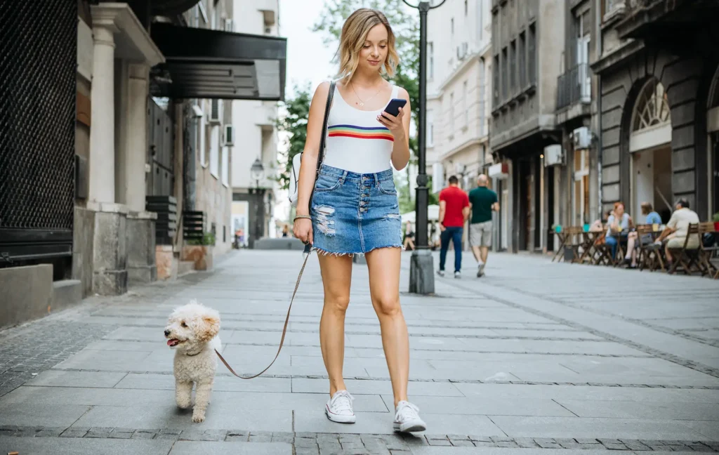 Woman looks at phone while walking dog