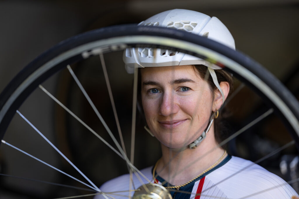 Woman stands smiling behind a bike wheel