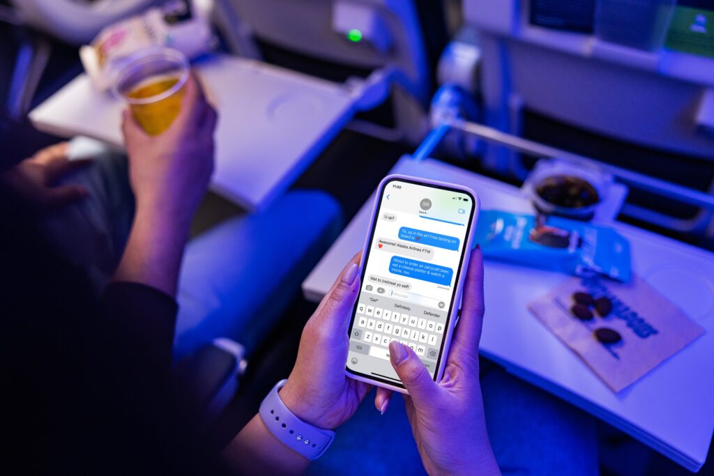 A mobile phone showing a text thread is held by a female passenger on an airplane.