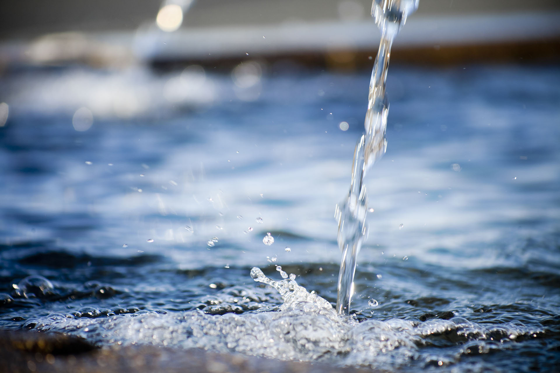 Close-up of a stream of water splashing into a clear blue pool.