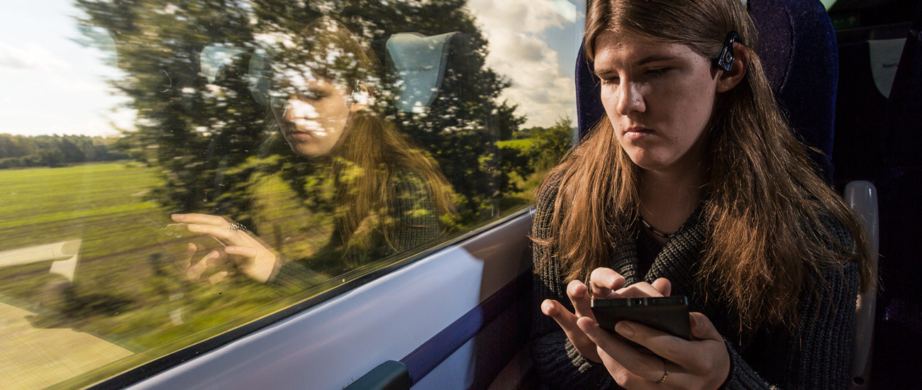 Jennifer Bottom sitting in the window seat using her phone to access Microsoft 3D soundscape technology on a train from Reading to London