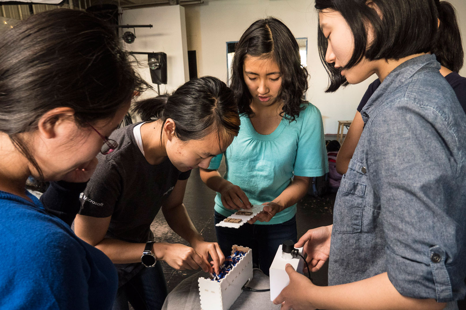 Photo of three students gathered around a fourth, who has her head down and is adjusting wires in the rectangular prototype