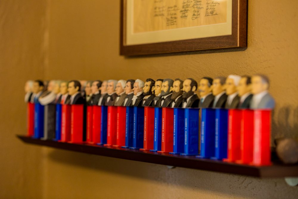 Blue and red Pez dispensers with busts of U.S. presidents are lined up in a row on a shelf in Gabe's room