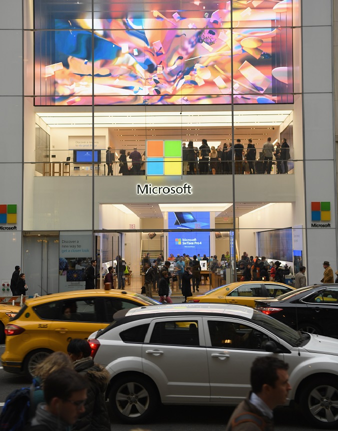 Busy street scene of cars and pedestrians in front of colorful digital art on Microsoft storefront