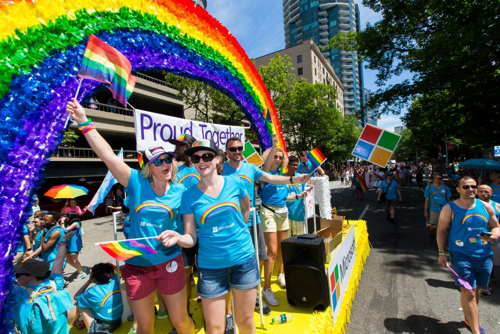 Photo of two women waving rainbow flags in front of Microsoft's float in the 2017 Seattle Pride parade