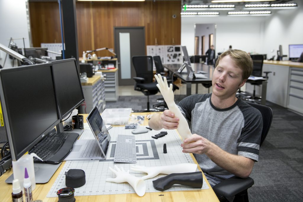 Easton LaChappelle holds one of the prototypes of his robotic arm while sitting at a desk.
