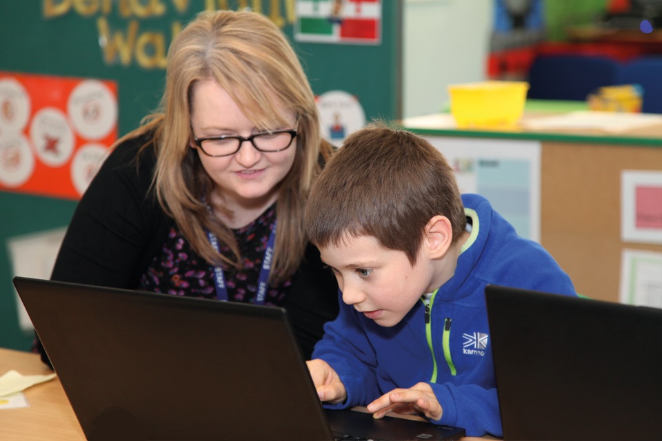 A teacher helps a boy use a laptop