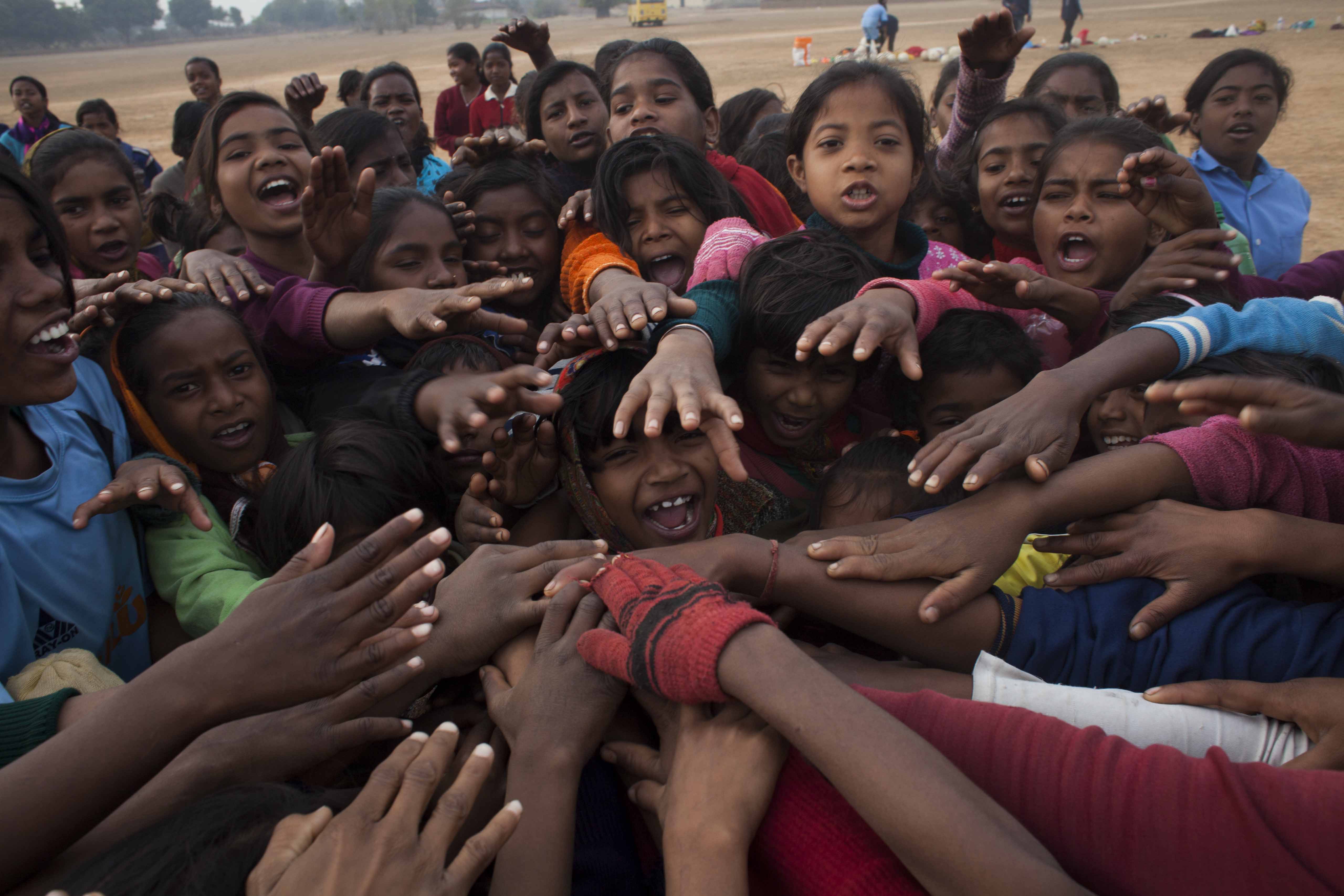 Dozens of young Indian girls press together, reaching their hands toward the middle of their huddle.