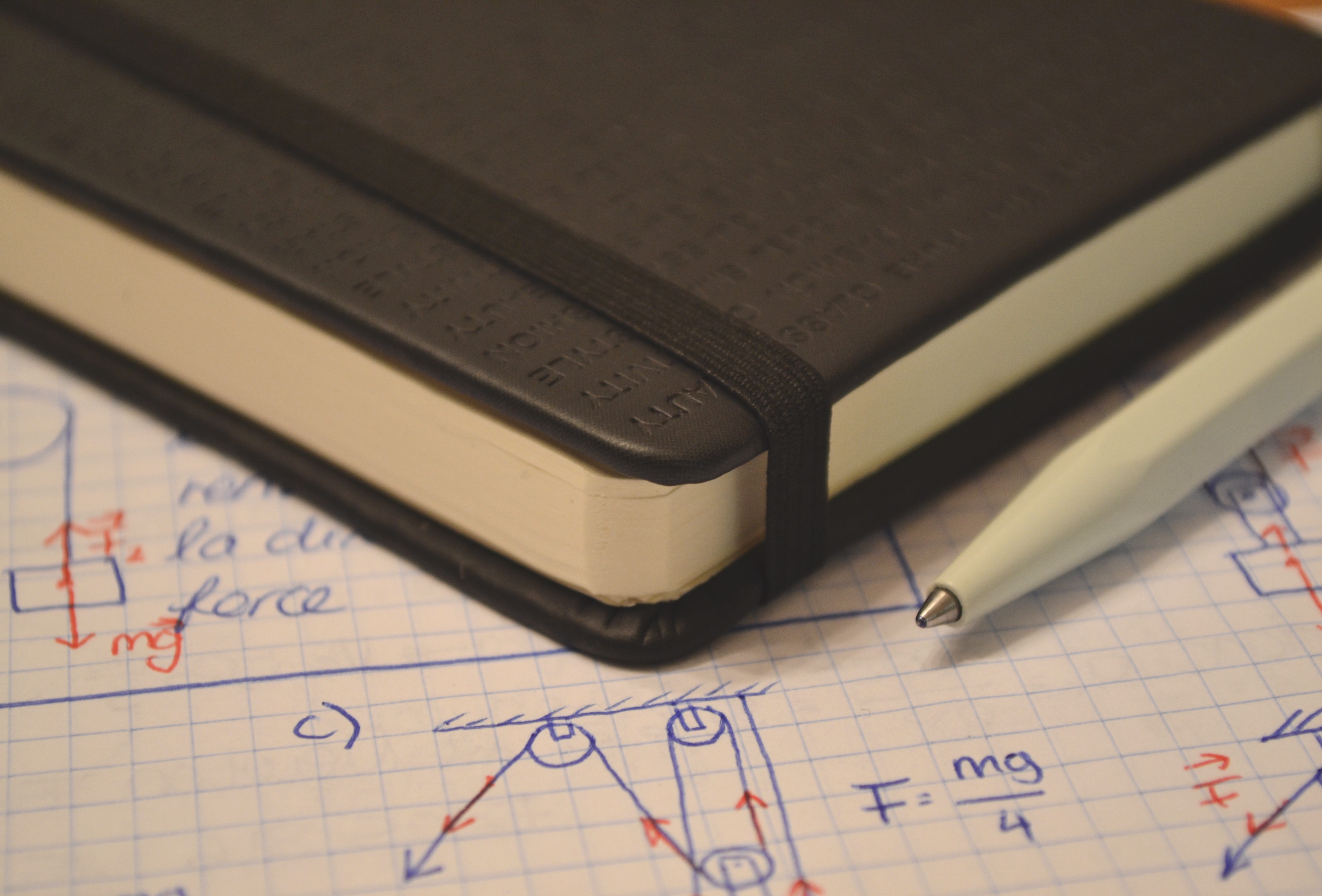 Notebook and pen laying on paper showing physics diagrams