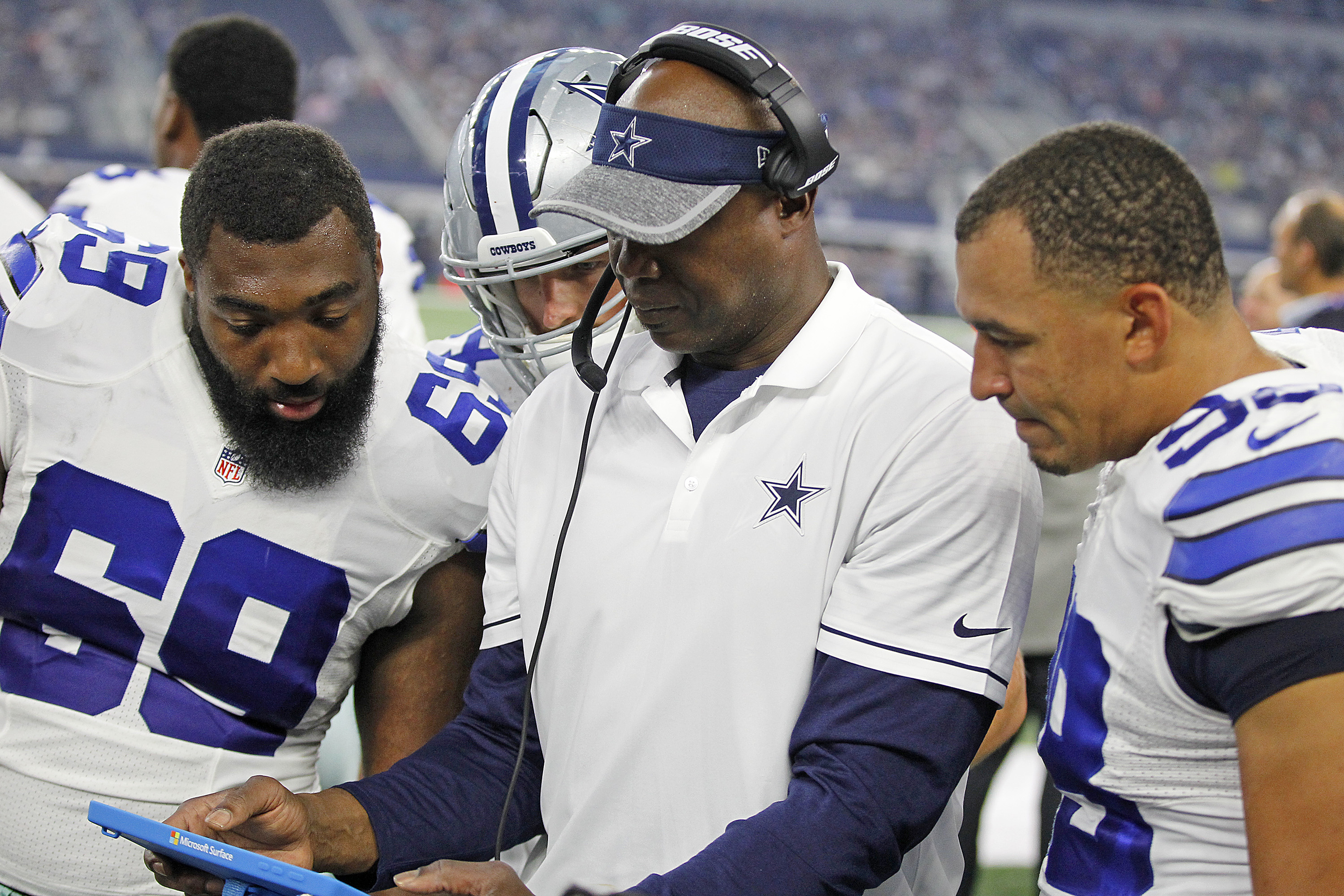 Three Dallas Cowboys players look over the shoulder of a coach holding a Surface Pro 4 tablet