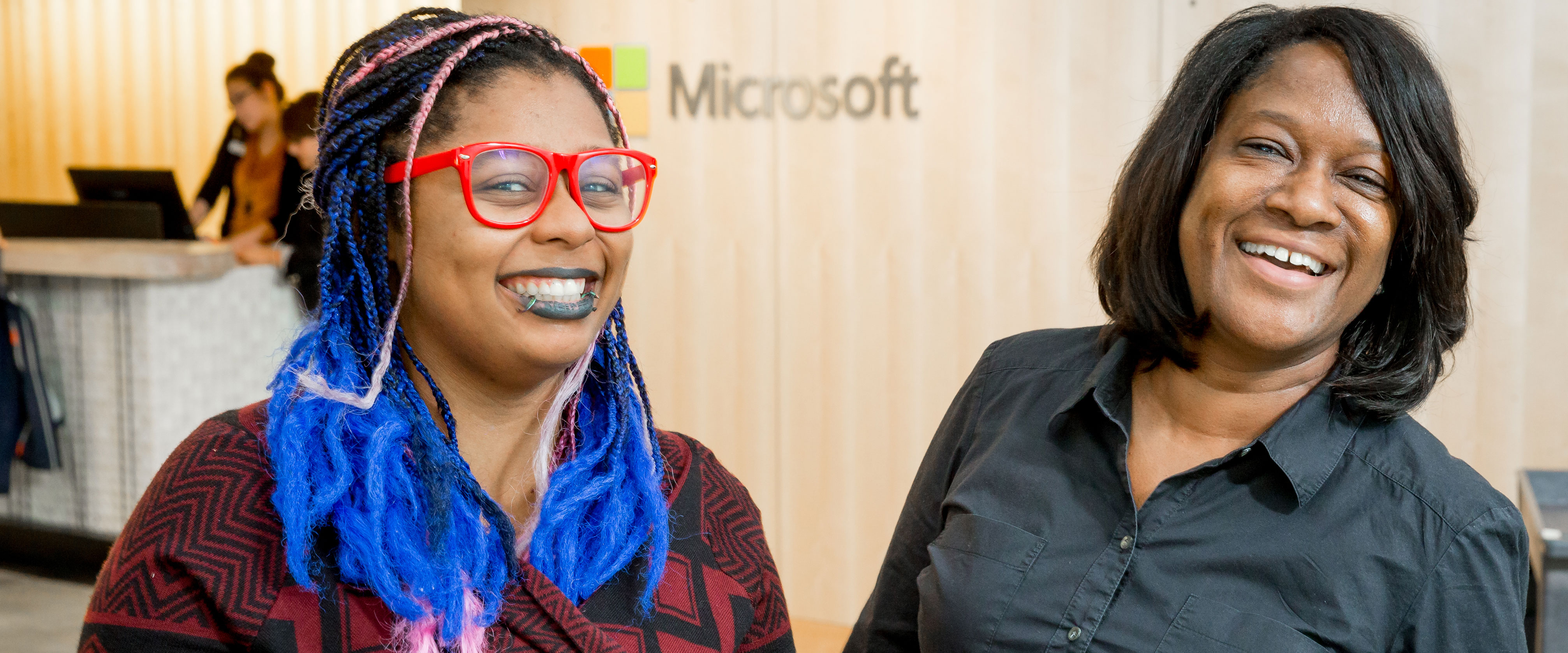 Photo of Kiara Blue and Jacky Wright smiling together in front of a wood-paneled wall with a Microsoft logo.