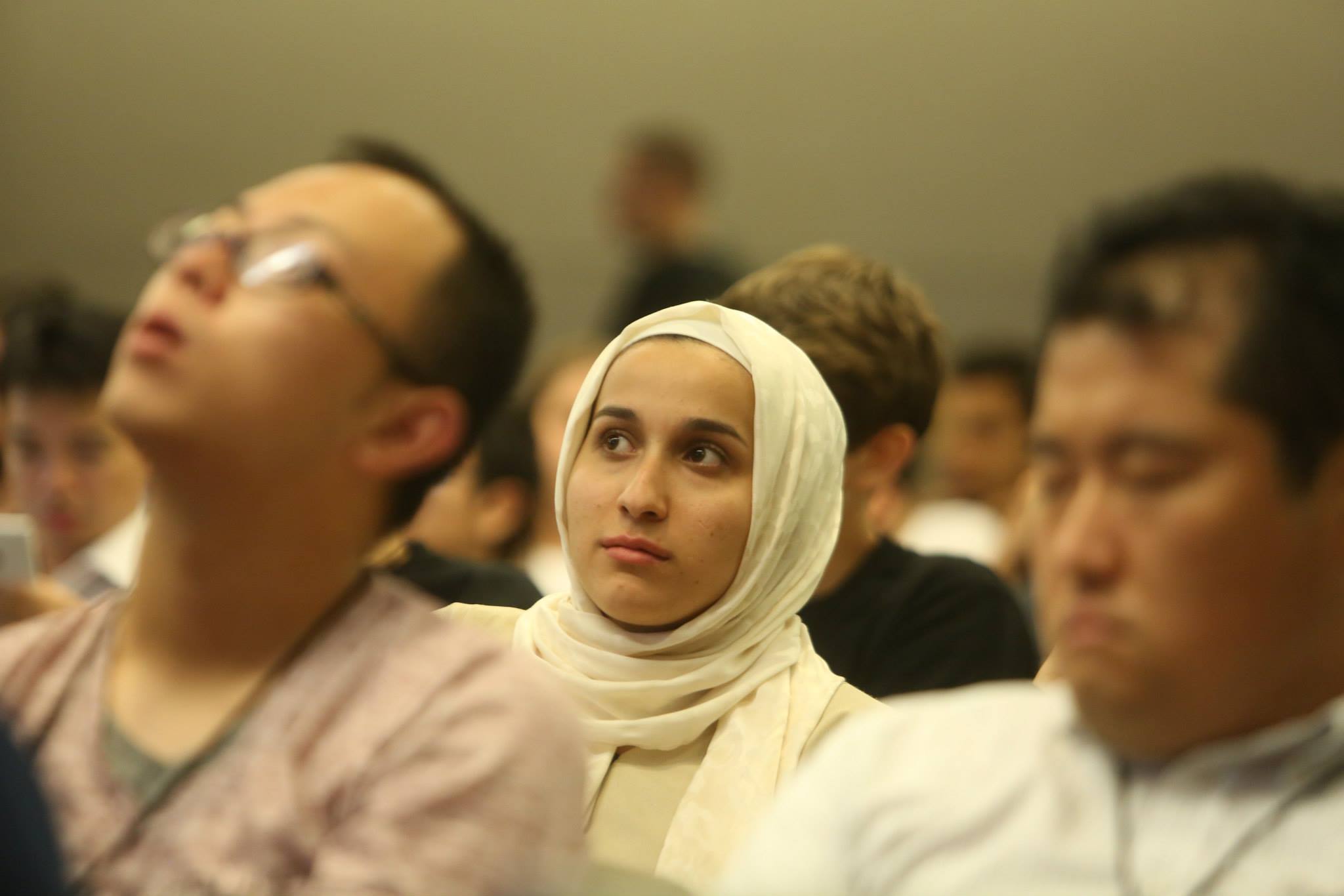 Woman in a white hijab in an audience listens to a session