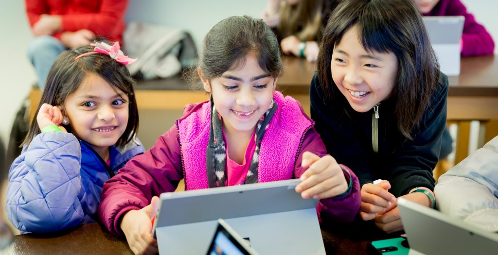 Photo of three smiling girls huddled around a Surface device