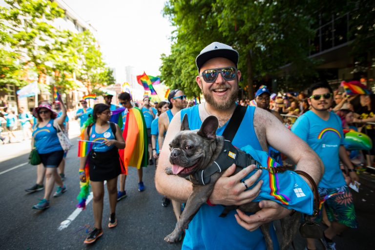 Photo of smiling man holding dog and walking in Seattle Pride parade