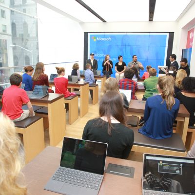 An audience of teenagers watch a presentation on stage in a Microsoft Store