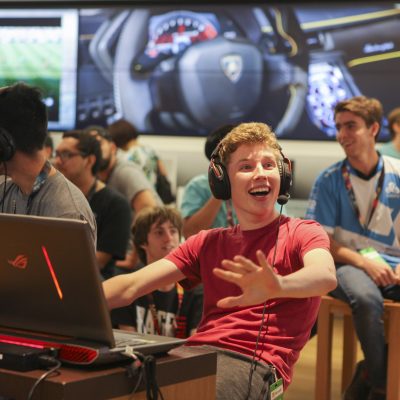 A smiling young man wears headphones and sits behind a laptop