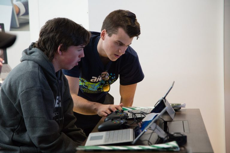 Two young men lean over a laptop screen