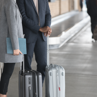 Two people stand with their suitcases at an airport curb
