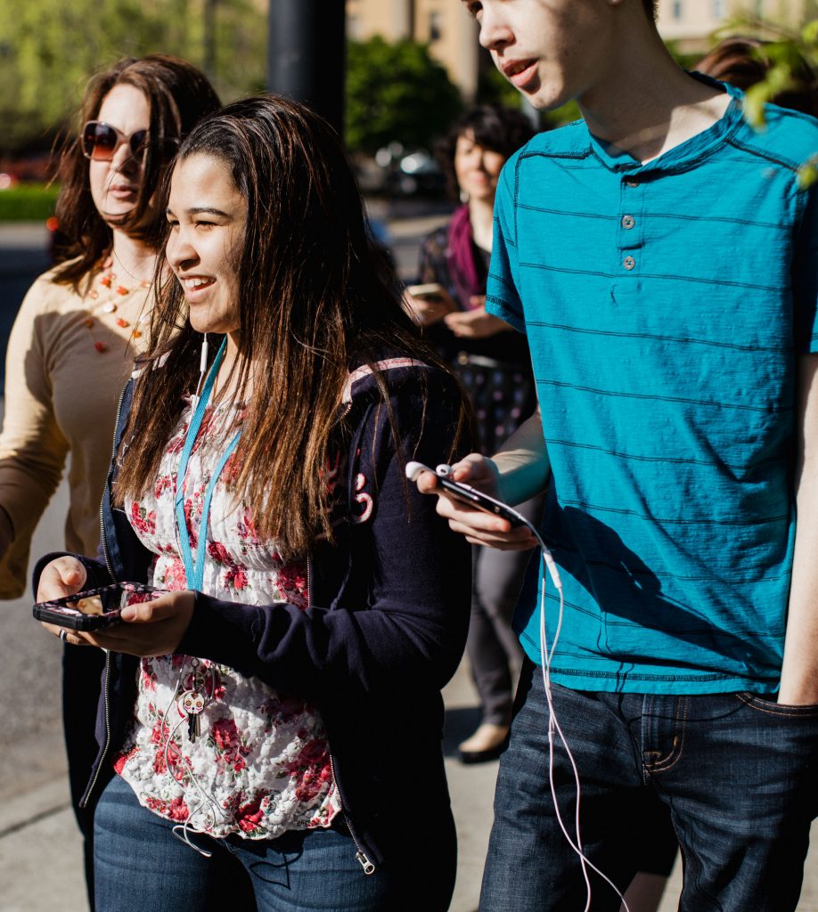 Smiling students walk in the sunshine with smart phones in their hands.