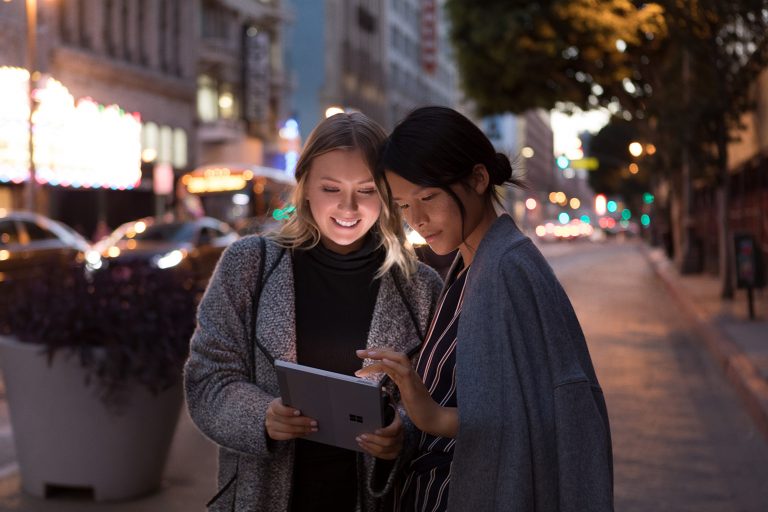 Two women use Surface Go on a dark street