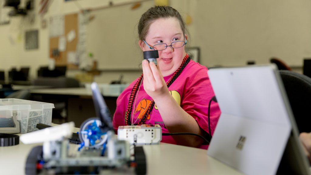 Photo of Pepper Swanson, member of a Unified Robotics team, holding up a wheel for her robot. 