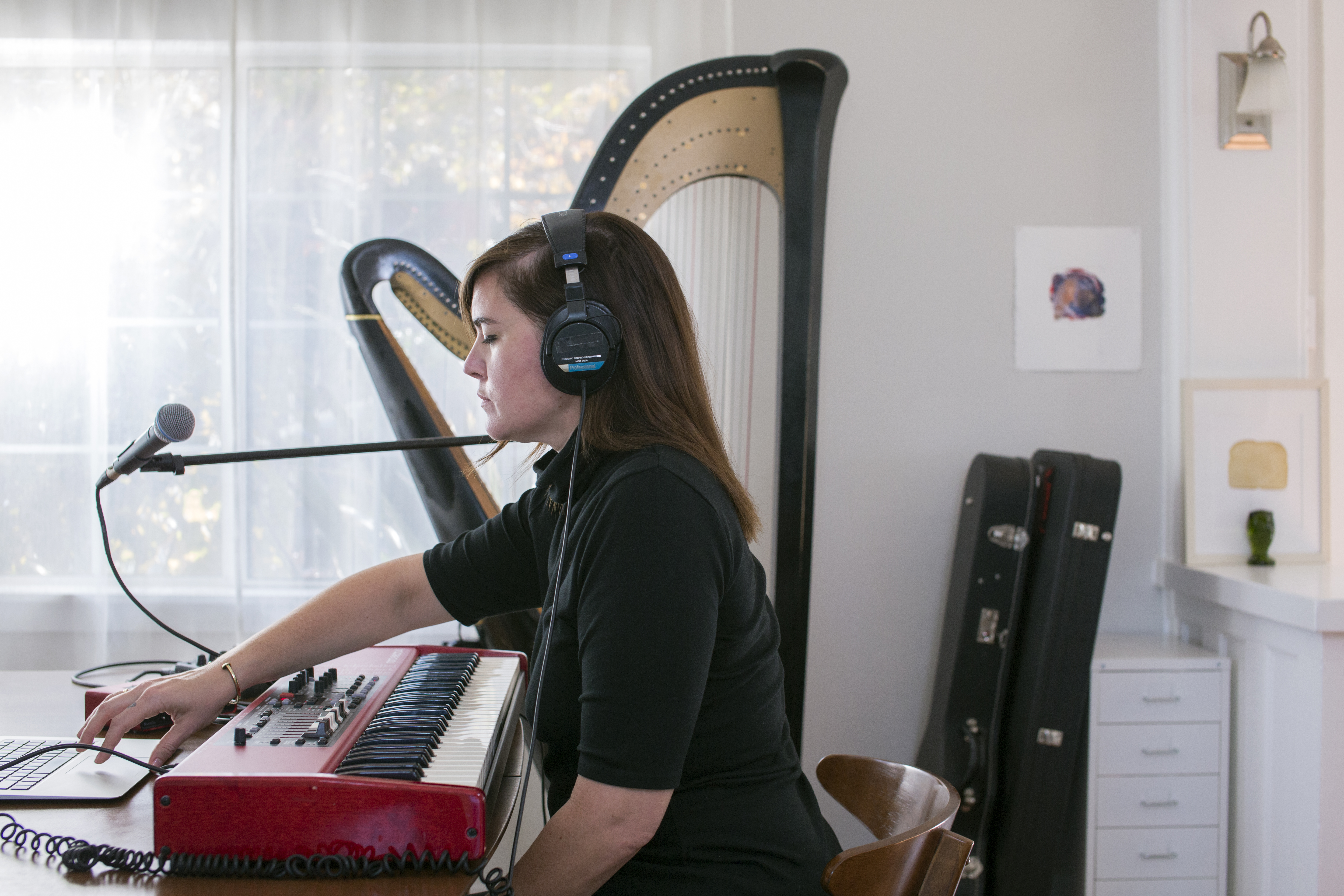 Woman wearing headphones interact with her laptop while she plays music with a harp in the background