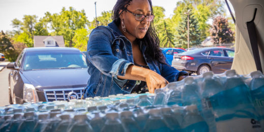 Woman loads cases of bottled water into a vehicle