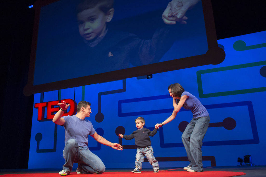 Photo of Roberto D'Angelo, Francesca Fedeli and their son Mario on stage presenting a TED talk