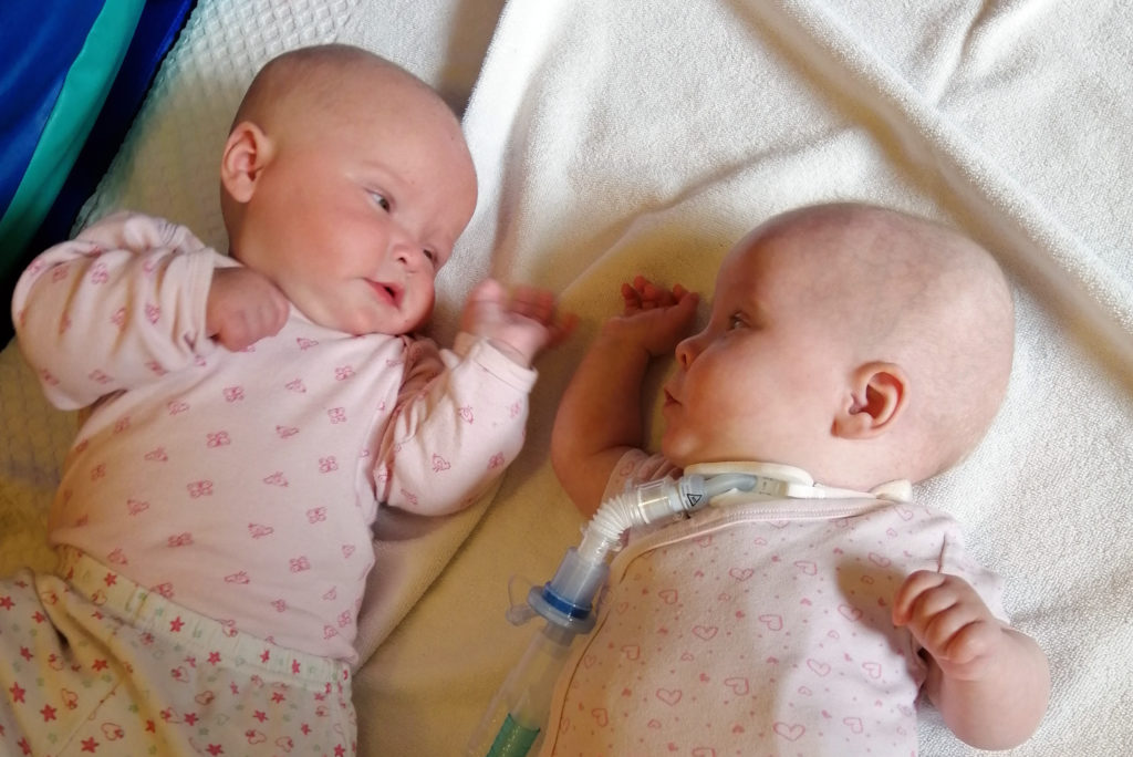 Twin baby girls look at each other in crib
