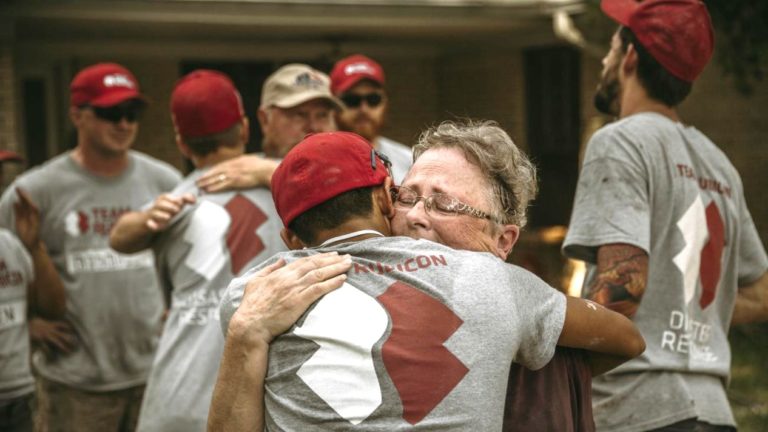 A young man wearing a Team Rubicon tshirt, hugs an older man.