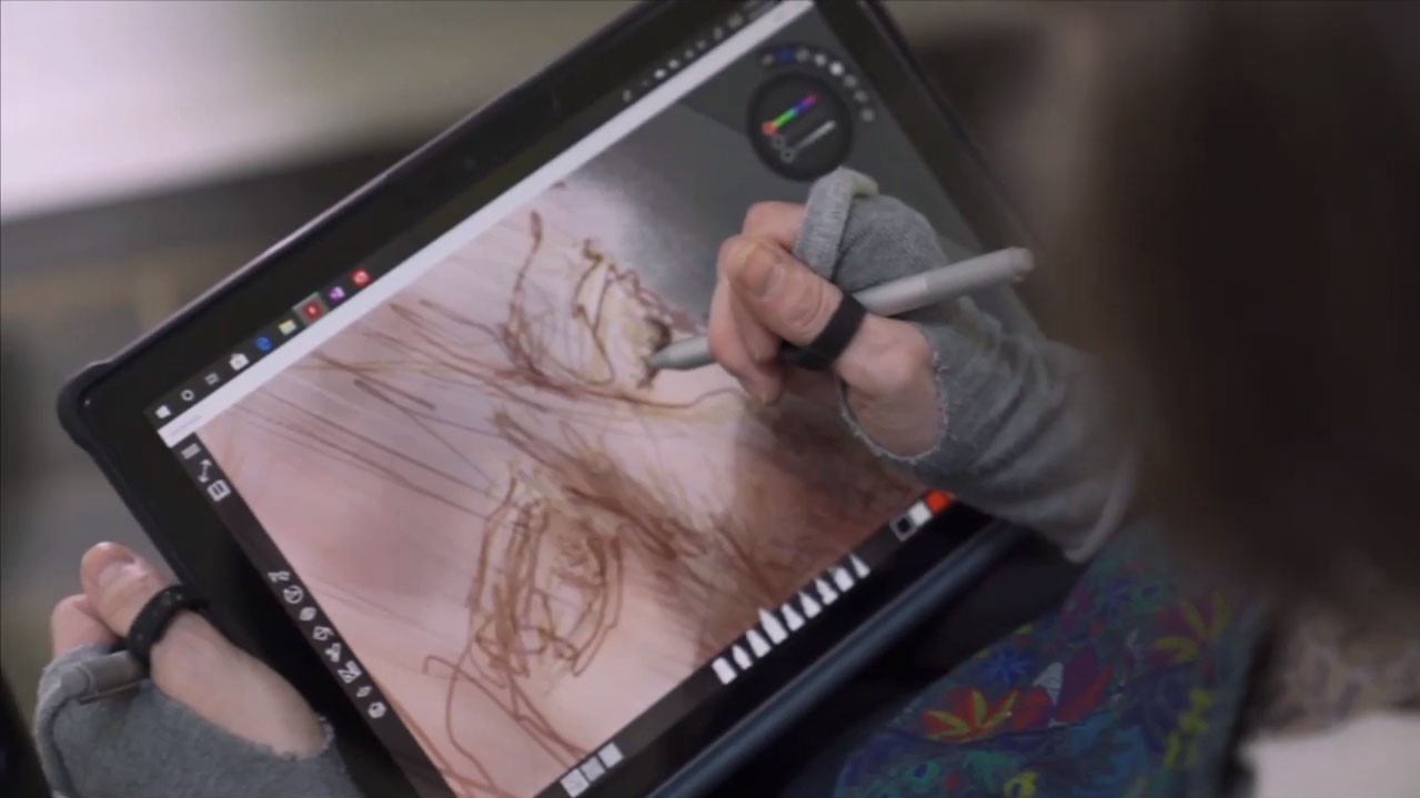 A woman's hand holds a stylus and creates an intricate, shaded drawing on the screen of a Surface device