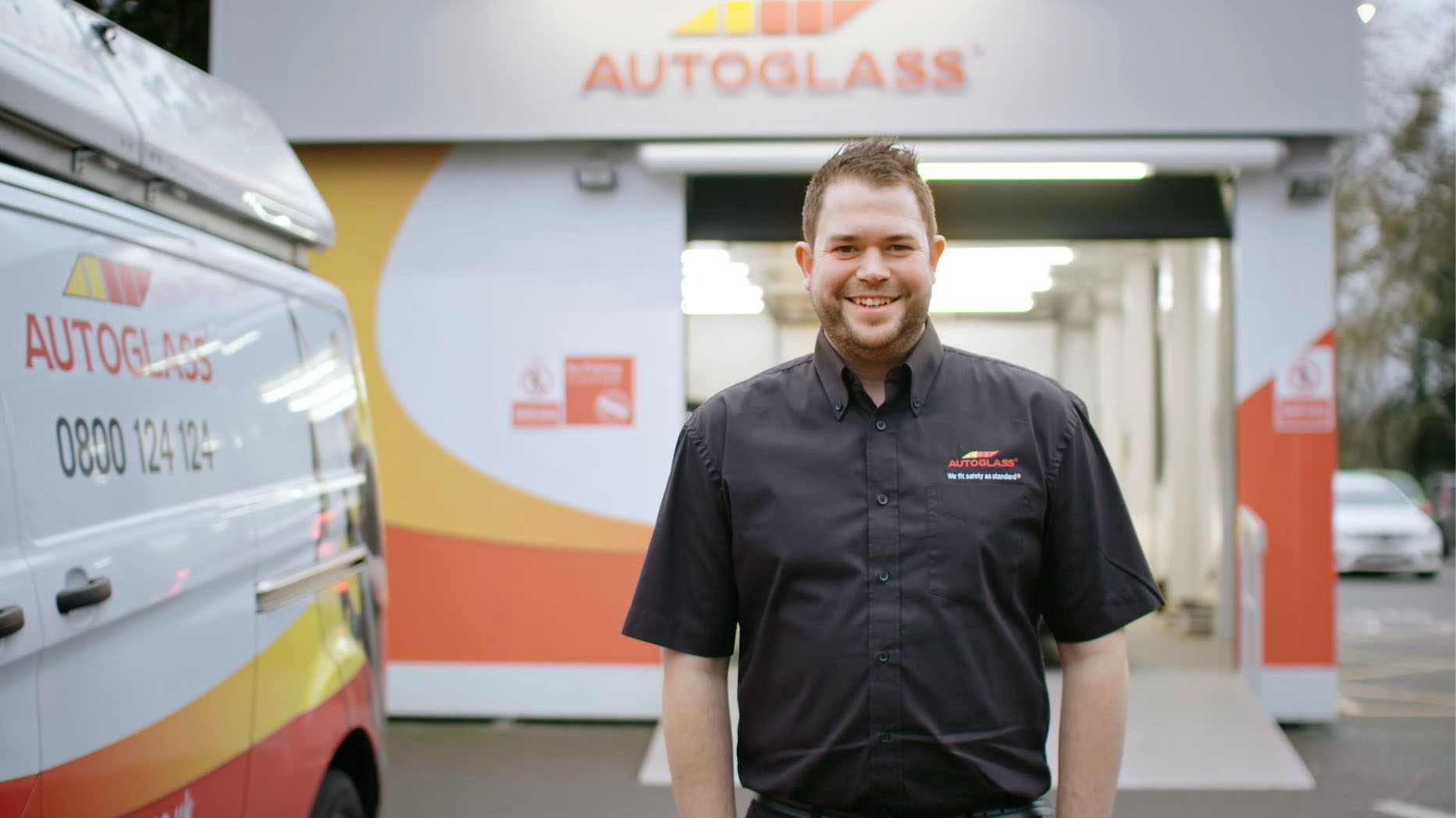 Man in a uniform stands in front of an Autoglass facility smiling