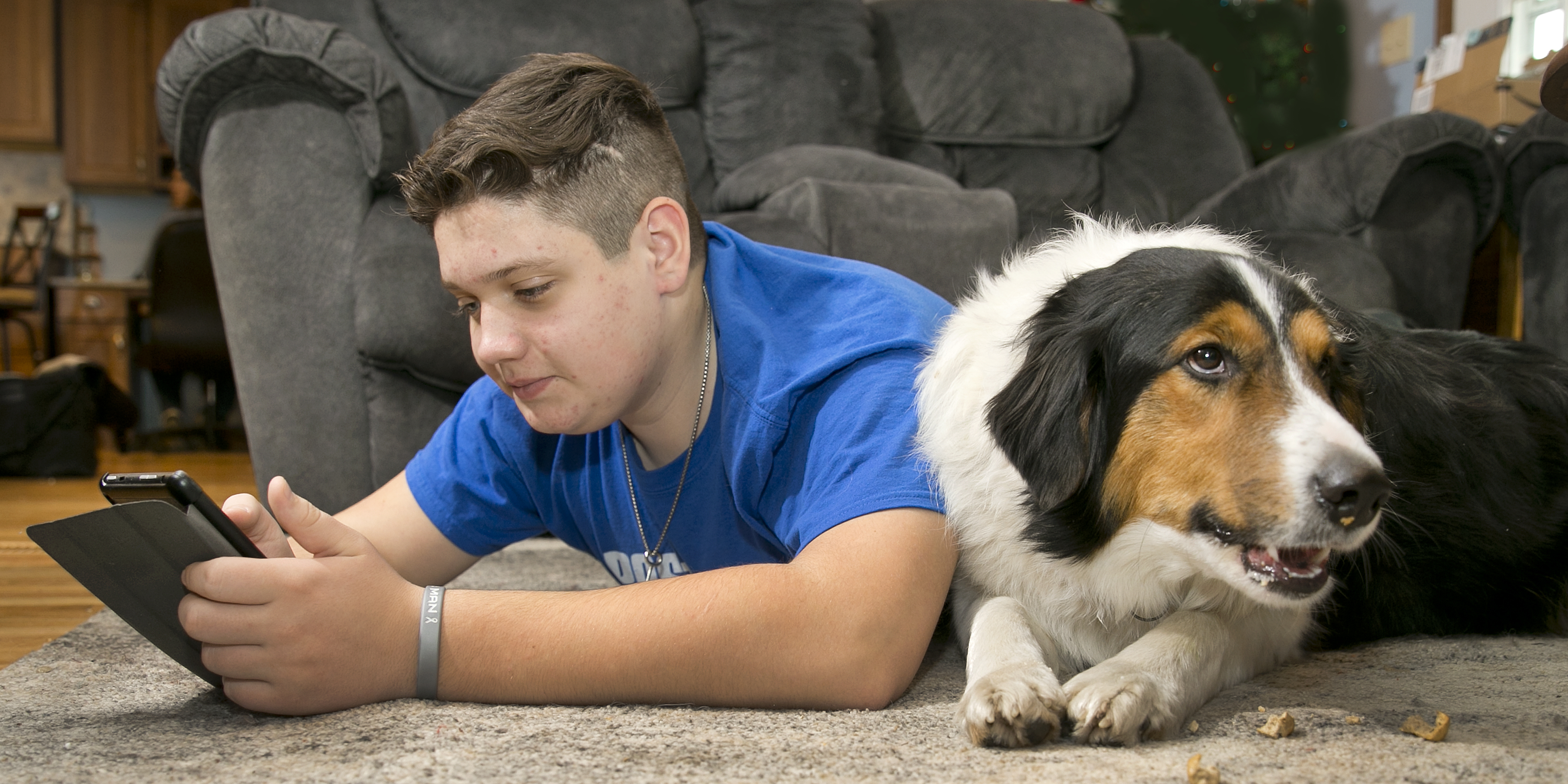 Boy interacts with his mobile phone while lying next to his dog on his living room floor
