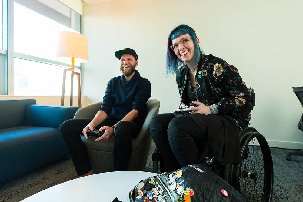 Two people, including one in a wheelchair, smile while holding game controllers and playing a video game