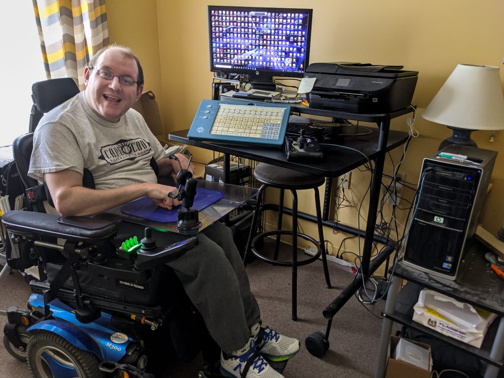A man in a wheelchair smiles in front of his computer