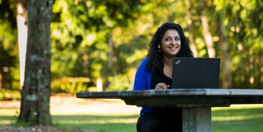 Woman smiles while working on her laptop near trees and grass