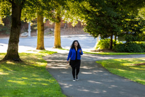 Woman walks near trees and grass park while talking on the phone