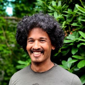 Man smiles in portrait against backdrop of green plants