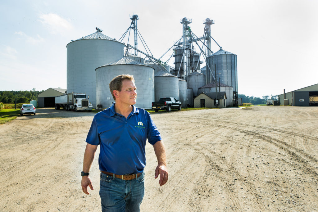 Portrait of Trey Hill, CEO of Harborview Farms in Rock Hall, Maryland, with a cluster of grain storage silos in the background.