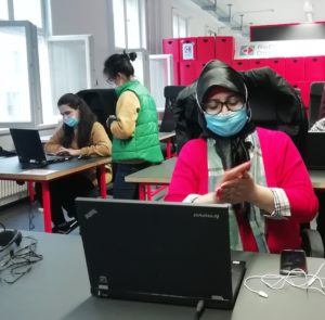 Students wearing masks sit in front of computers in a classroom