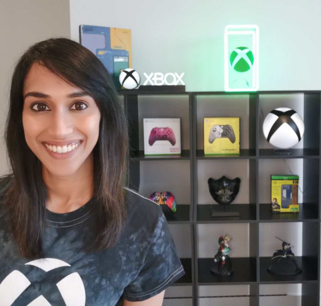 Dhayana Sena wearing an Xbox shirt in front of a shelf with Xbox controllers