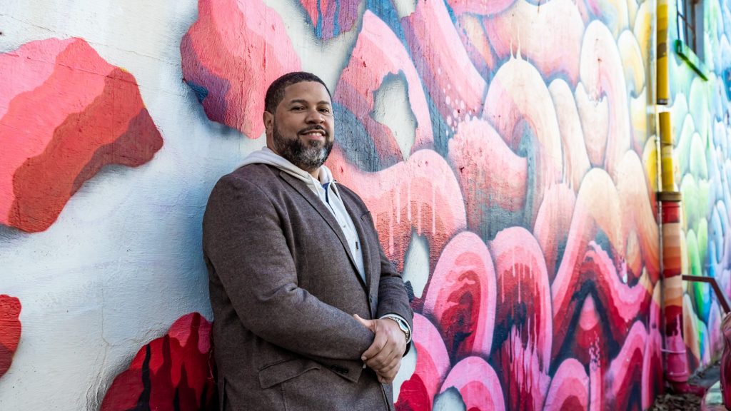 Man stands in front of colorful mural