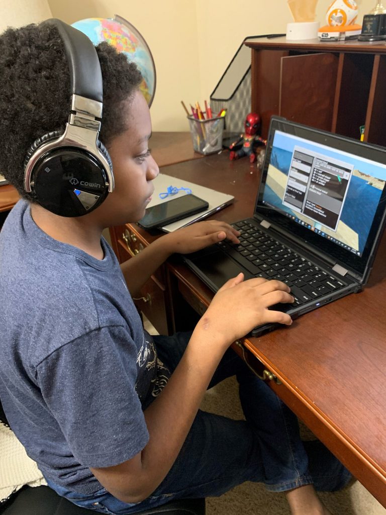 Child wearing headphones plays Minecraft on a laptop on a desk