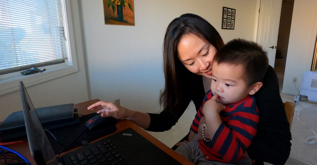 A mother in front of a computer smiles with her son young