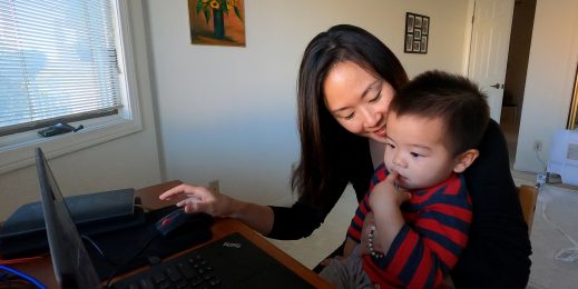 A mother in front of a computer smiles with her son young