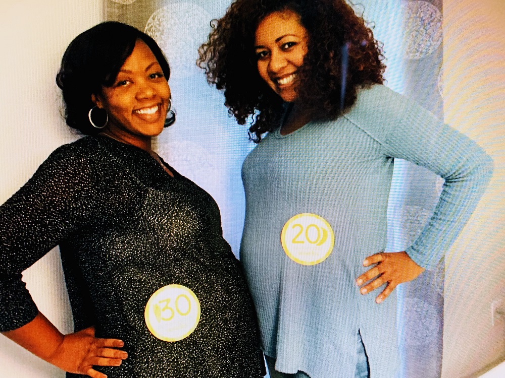 Two pregnant friends smile and pose with bellies toward each other